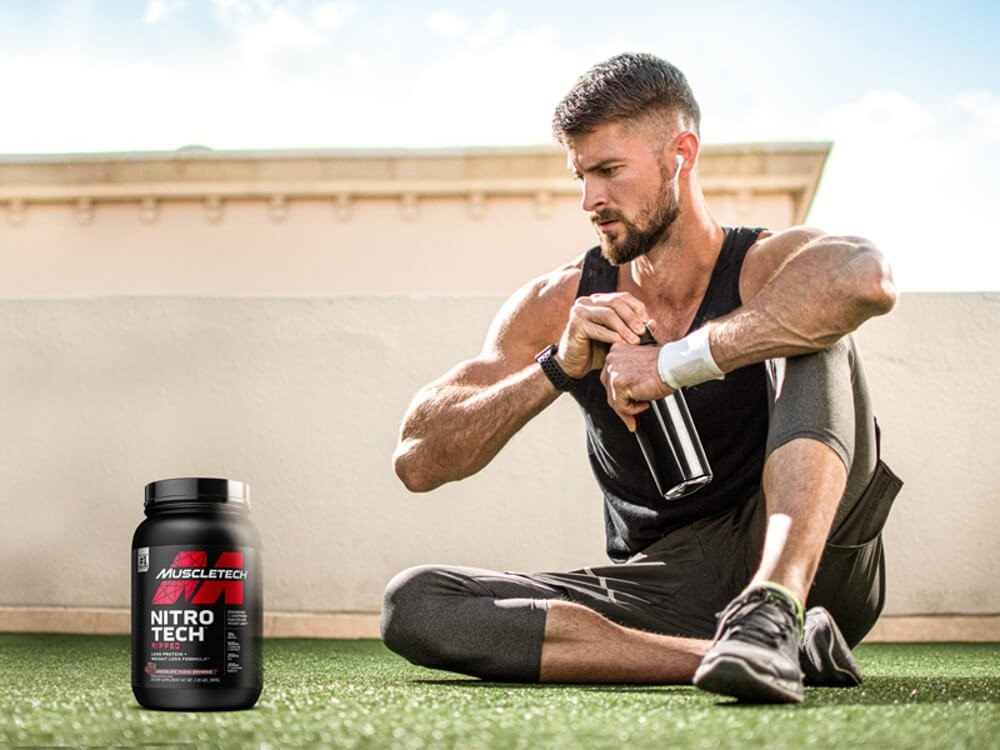 Hombre sentado junto a la botella de Nitro Tech Whey Protein Gold Powder